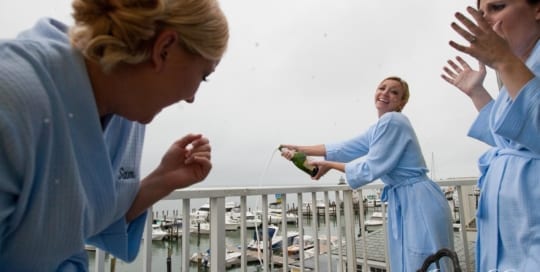 Woman opening champagne on deck overlooking marina.