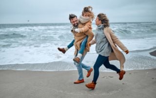 A mom, dad, and daughter run on the beach during the winter in Old Saybrook, CT.